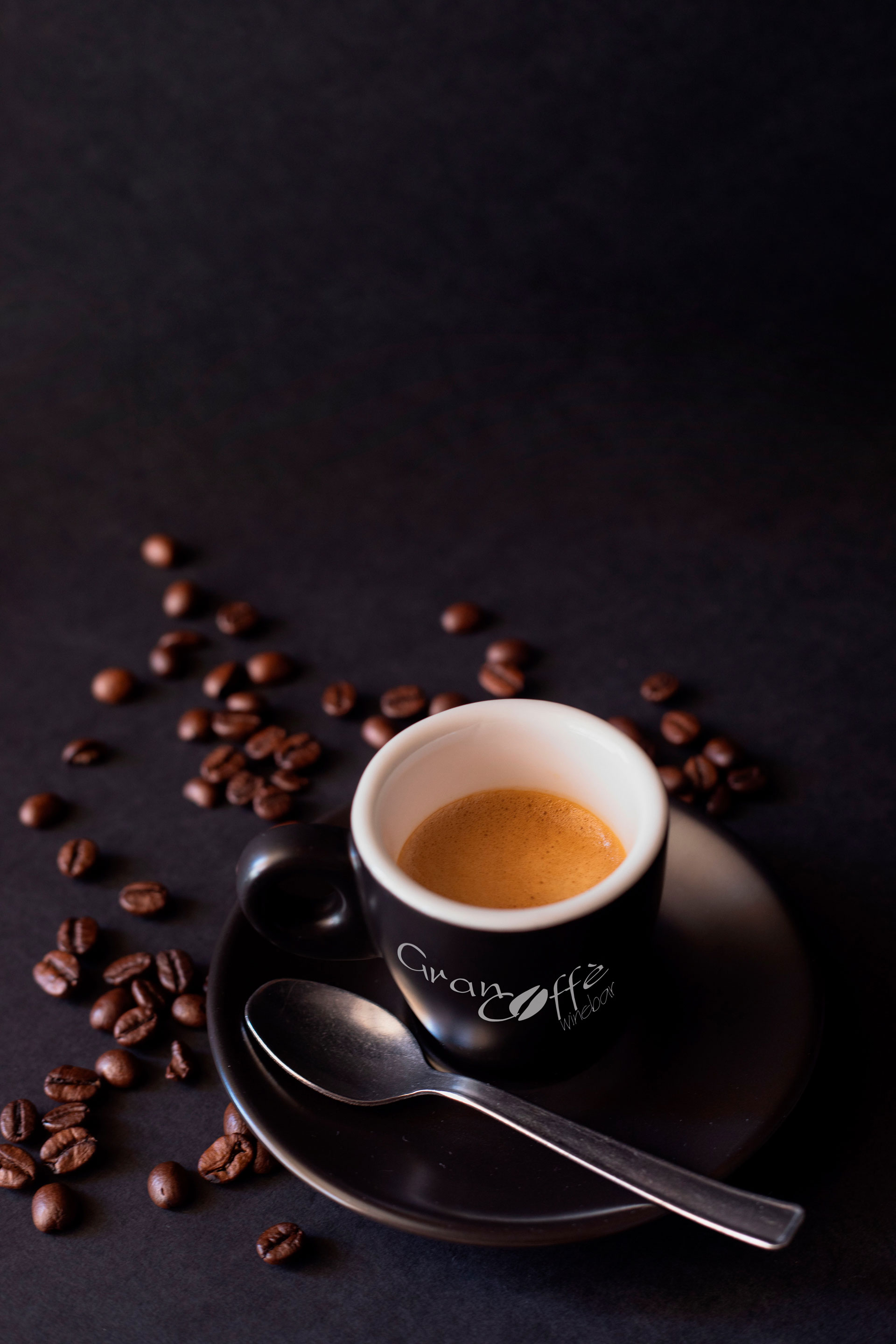 Tazzina nera di caffe con chicchi su fondo scuro